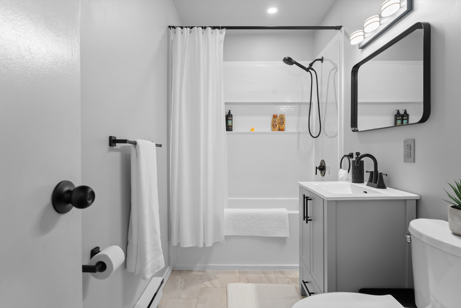 Renovated bathroom — full view of the tub, shower, and grey vanity