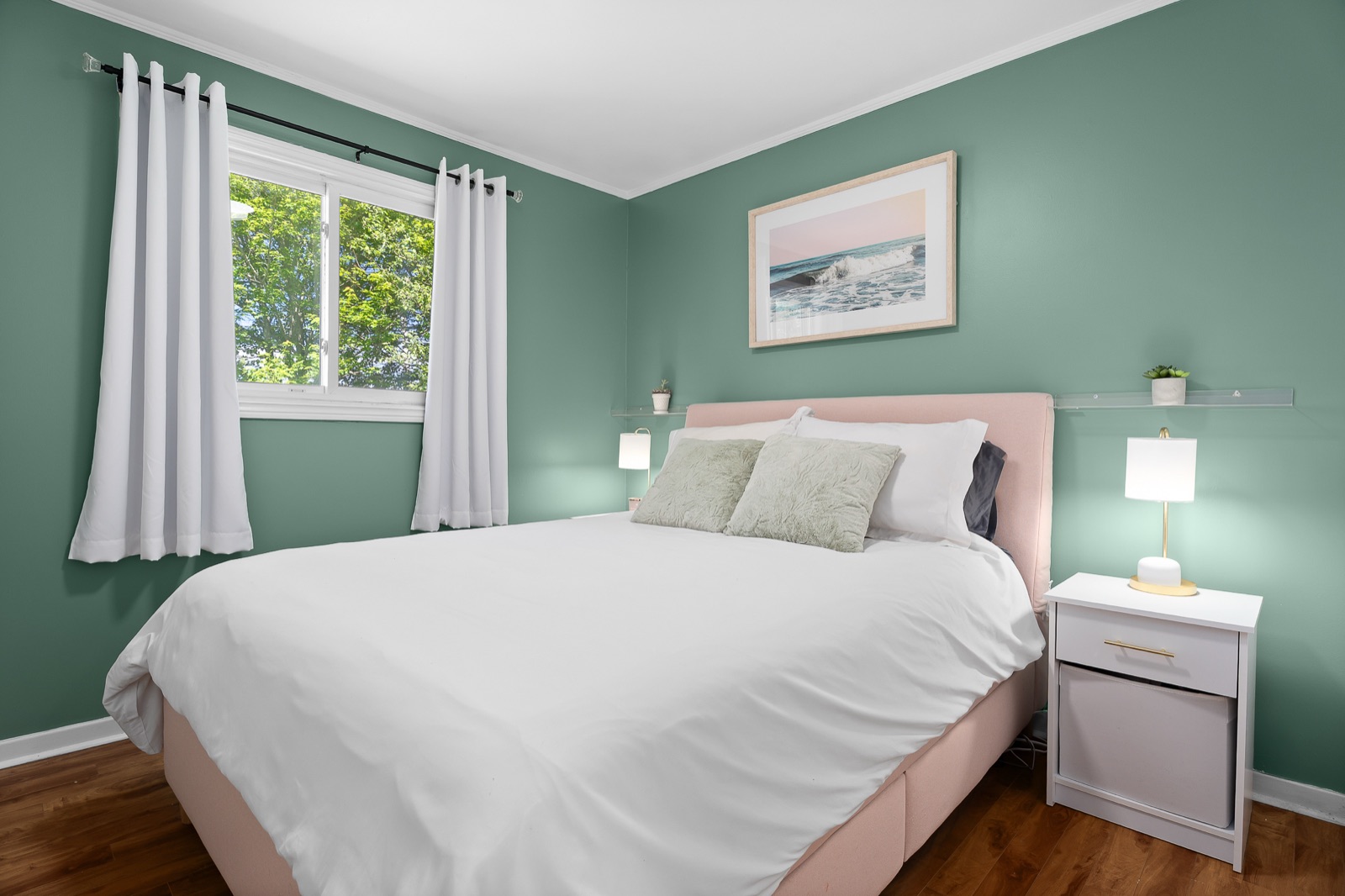 Green-walled bedroom with a blush bed and coastal artwork